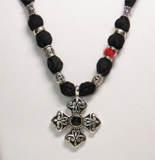 This necklace has cotton fabric with a black background and tiny gray flowers.  
The cross pendant is black and silver tone metal with a black faceted piece in the center.  The beads are silver tone metal and the whole black and silver look is accented with one red glass bead with pretty designed colors throughout.