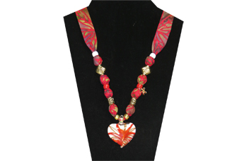 This necklace has a pretty red and white glass heart pendant. The beads are gold tone metal and it has a gold tone flower charm. The fabric is a cotton multi-colored red with purple olive leaf pattern.