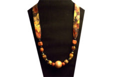 This necklace has a large round light wooden bead in the center and smaller red square beads on the ties. The fabric is cotton with a fall color leaf pattern.