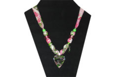 This dainty necklace has a clear glass heart pendant with pink and green lines criss-crossing through it. The fabric has a pink, white and green paisley pattern and is silky. The accent beads are green glass with painted pattern, pink faceted, delicate green rhinestone, and silver tone metal. There is a delicate green faceted charm hanging too.