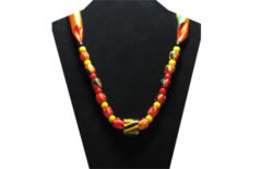 This brightly colored necklace has a clear large barber pole glass bead with stripes of yellow, blue and red inside it. The fabric is silky yellow, orange, red and green with red and yellow pony beads.